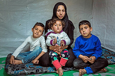 Flüchtlingsfamilie auf Bodenmatte vor Plane