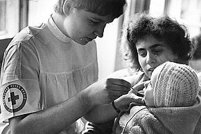historisches Foto: Rotkreuzschwester verabreicht einem Baby Medizin