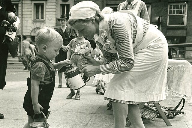 Kleiner Junge wirft Geld in Spendendose einer DRK-Helferin