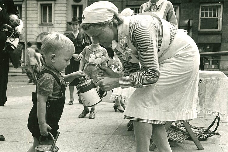 Kleiner Junge wirft Geld in Spendendose einer DRK-Helferin