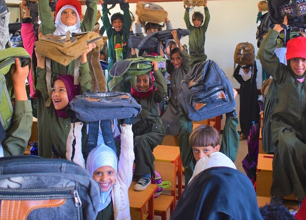 Schulkinder halten lachend ihre neuen Schulranzen in die Luft
