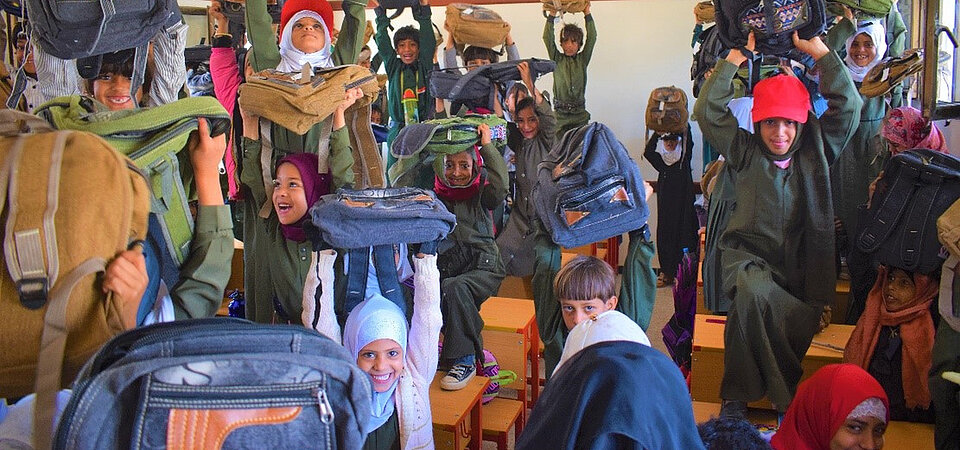 Schulkinder halten lachend ihre neuen Schulranzen in die Luft