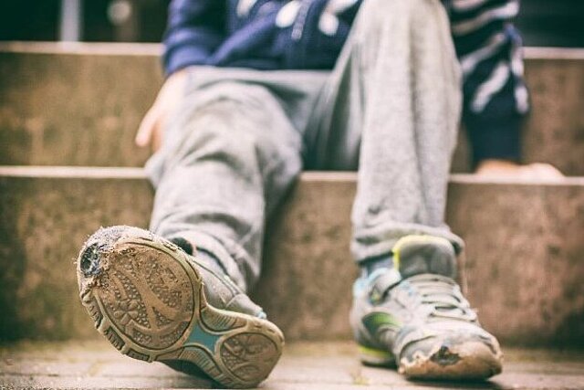 Auf dem Bild sind zwei Kinderbeine zu sehen, die mit abgewetzten Turnschuhen auf einer Treppe sitzen