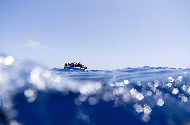 Man sieht im Vordergrund die Meereswellen, im Hintergrund ein kleines Boot.