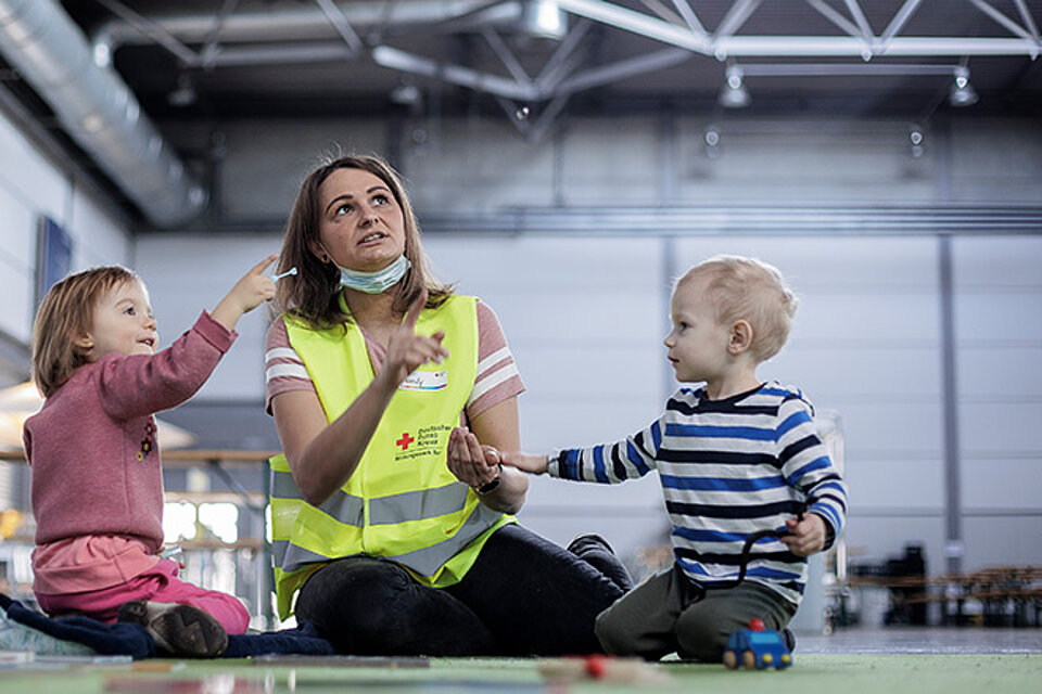 DRKlerin spielt mit zwei Kleinkindern