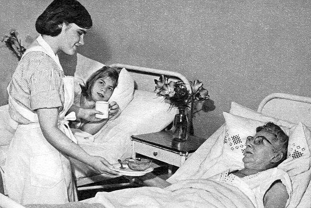 Junge Frau in Uniform am Bett zweiter Patientinnen