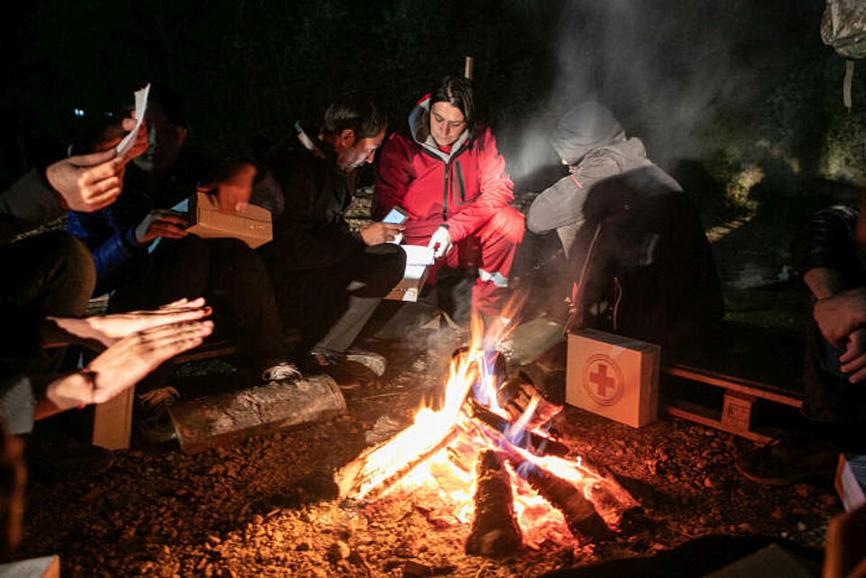 Rotkreuzhelfer mit Geflüchteten an einem Feuer