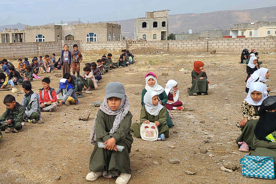 Schulkinder sitzen im Freien auf der Erde