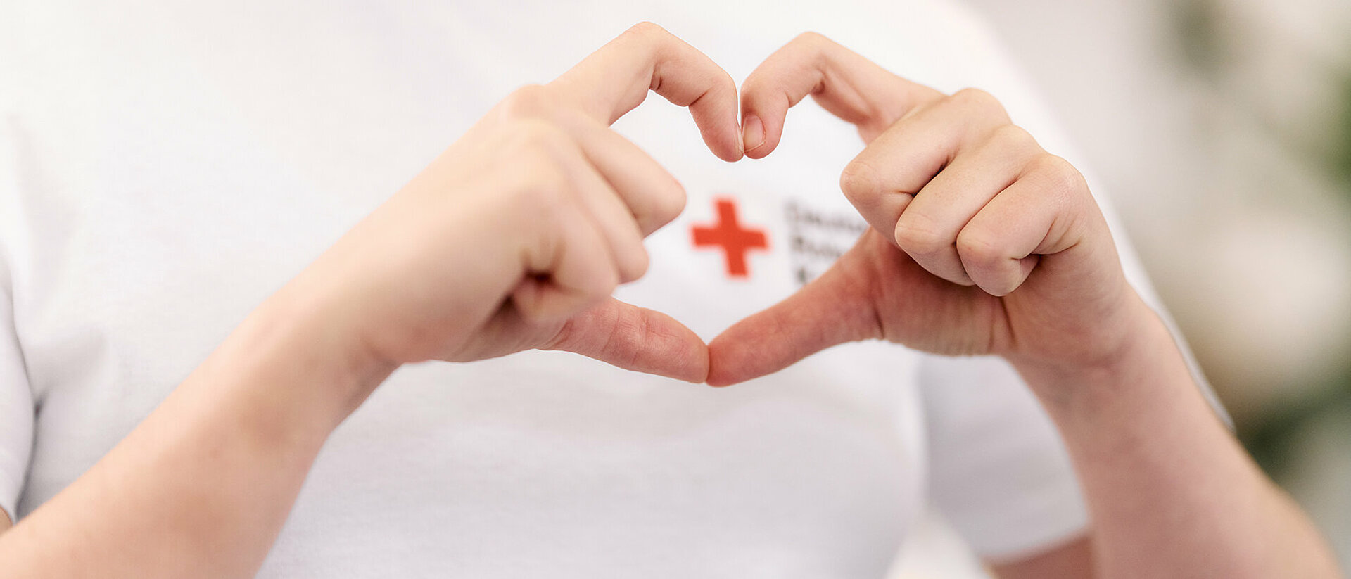 Corporate Volunteering in Form von Spenden: Hände formen ein Herz um ein DRK-Logo