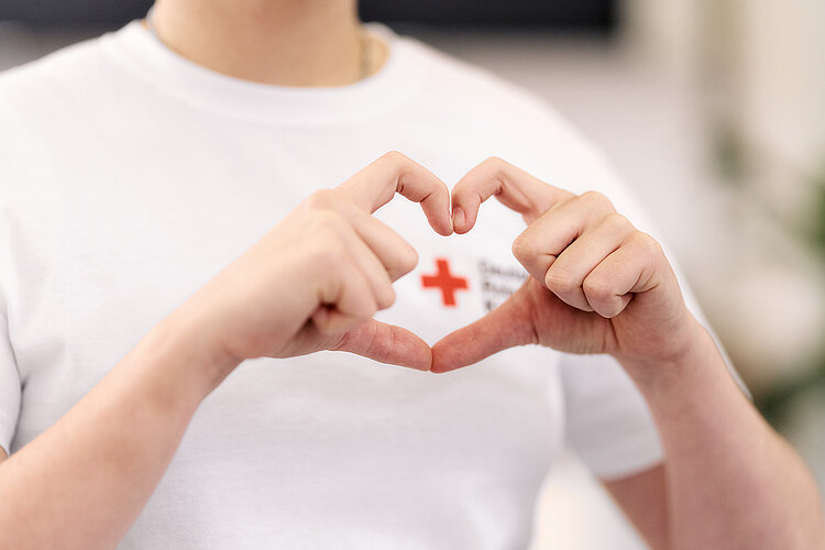 Corporate Volunteering in Form von Spenden: Hände formen ein Herz um ein DRK-Logo