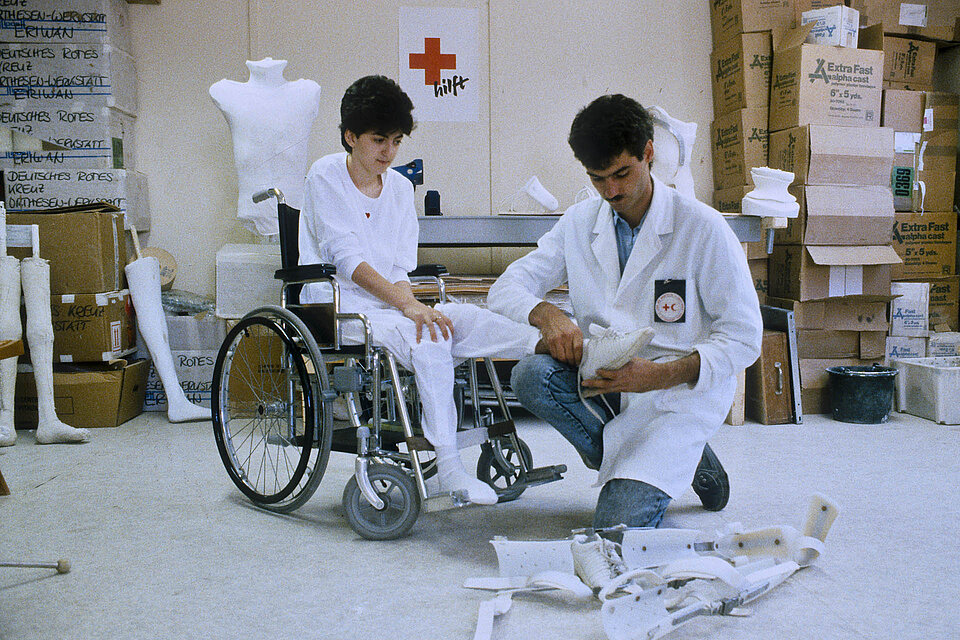 Junger Mann passt Beinprothese bei junger Frau im Rollstuhl an