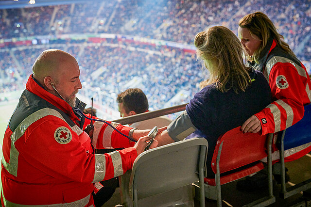 DRK-Sanitäter misst den Blutdruck bei einer Zuschauerin im Stadion