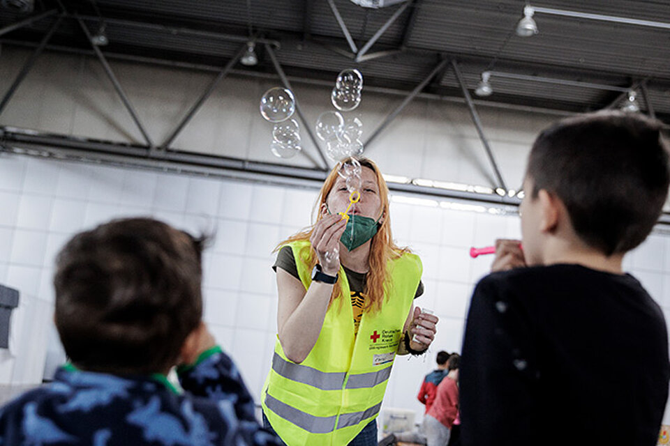 DRKlerin macht Seifenblasen für zwei ukrainische Kinder