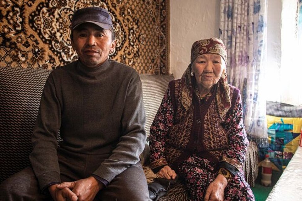 Mann und Seniorin sitzen vor Wandteppich