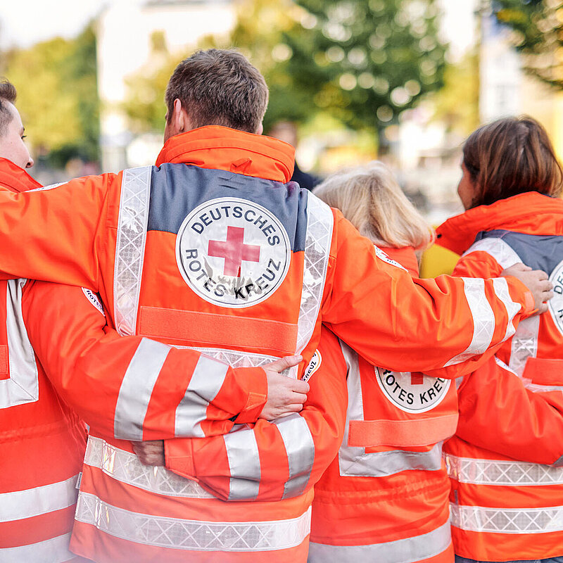 Vier DRKler in Einsatzjacken legen Arme über Schultern