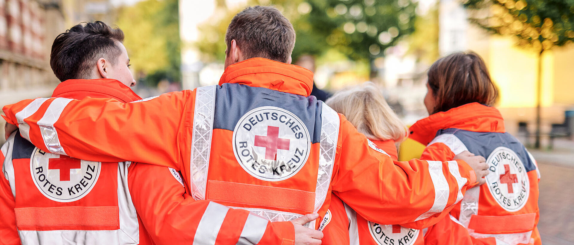 Vier DRKler in Einsatzjacken legen Arme über Schultern