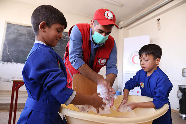 SARC-Helfer übt mit zwei Jungen Händewaschen