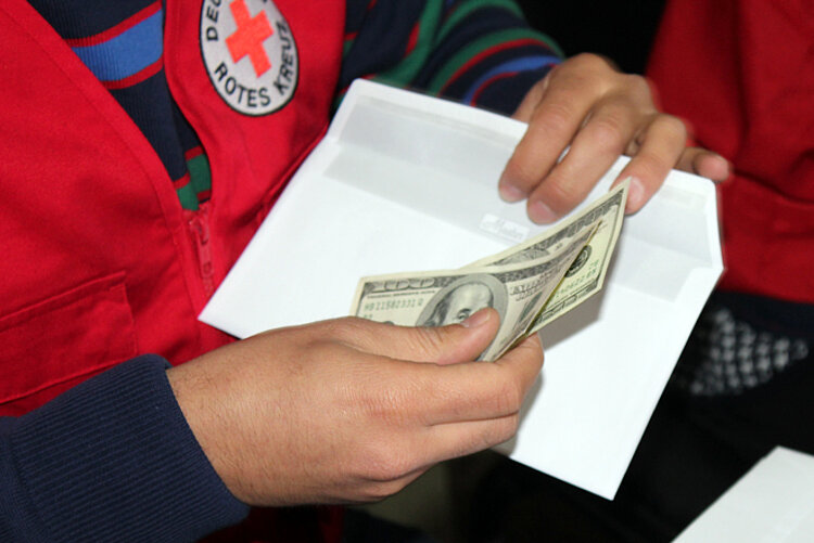 Foto: DRK-Mitarbeiterin hält Geldscheine und einen Briefumschlag in der Hand - Detailaufnahme