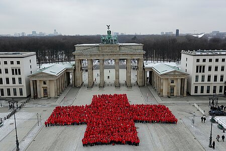 Viele Menschen in roten Jacken bilden vor dem Brandenburger Tor ein großes Rotes Kreuz