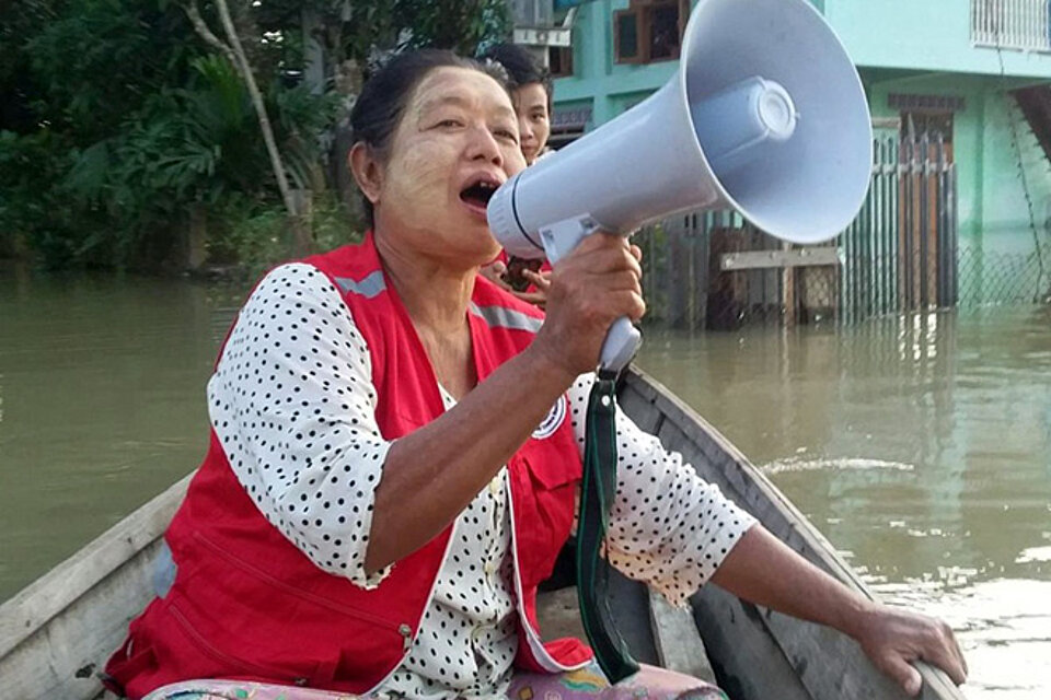Nach Überschwemmung: Rotkreuzhelferin des Myanmarischen Roten Kreuzes auf Boot mit Megafon