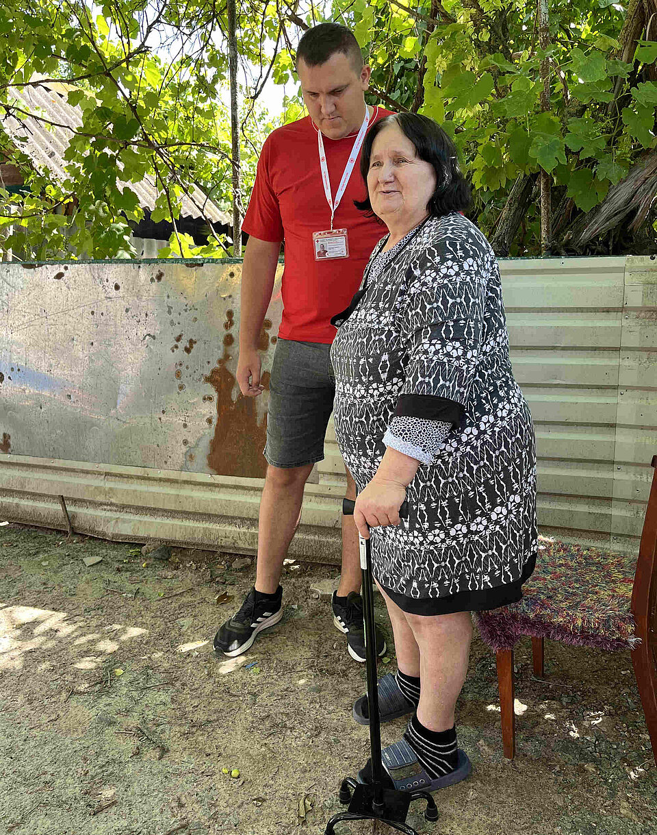 Ein Rotkreuzmitarbeiter hilft einer Frau mit einer Gehhilfe