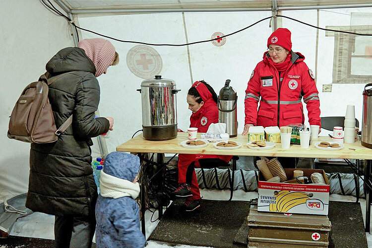 Frau mit Kind wärmt sich in Zelt des Ukrainischen Roten Kreuzes auf