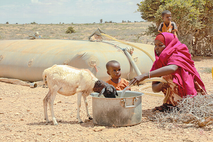 Wasserstelle in Somalia während der Dürrezeit Frau mit Kind und Nutztier an einer Wasserstelle in Somalia