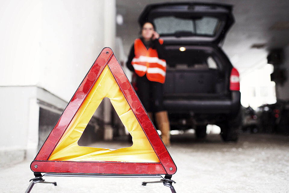 Warndreieck vor Auto und telefonierender Frau