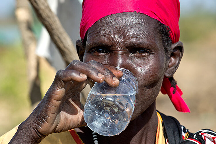Südsudanische Person trinkt Wasser aus einer scharfkantigen Wasserflasche