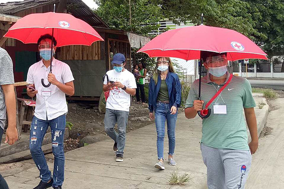 Philippinische Freiwillige laufen mit Rotkreuzregenschirmen 