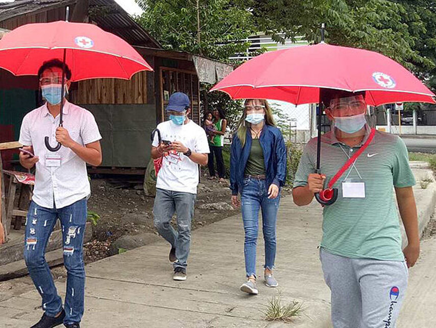 Philippinische Freiwillige laufen mit Rotkreuzregenschirmen 