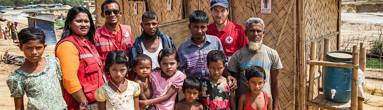 Ein Gruppe von Flüchtlingen im Flüchtlingscamp Cox's Bazar, Bangladesch, mit Helferinnen und Helfern des Roten Kreuzs und Roten Halbmondes