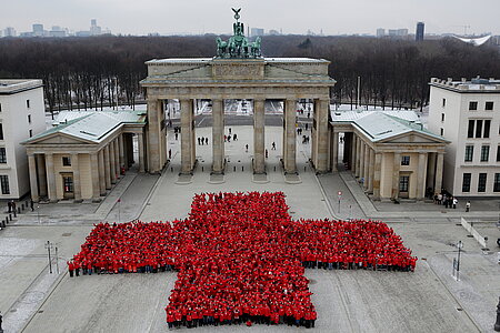 Menschen bilden vor dem Brandenburger Tor in Berlin ein großes rotes Kreuz.