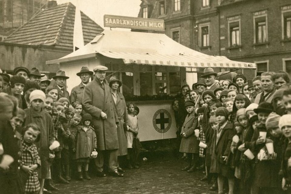 Ausgabe von Milch an Bedürftige durch das DRK: Stand des DRK in Saarbrücken, umringt von Bevölkerung - 1920er Jahre