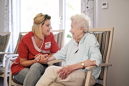Eine Pflegemitarbeiterin des DRK sitzt bei einer zu pflegenden Person und wendet sich ihr zu.