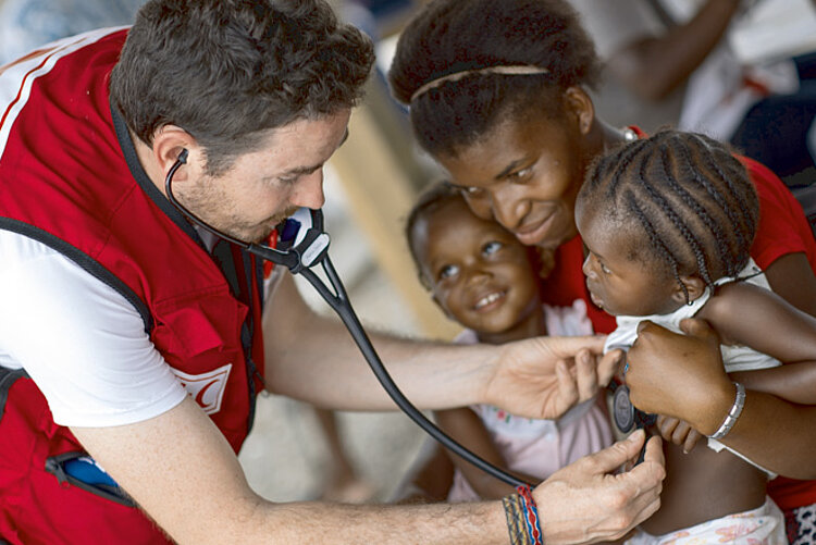 Foto: Arzt untersucht ein Mädchen auf dem Schoß ihrer Mutter in Haiti