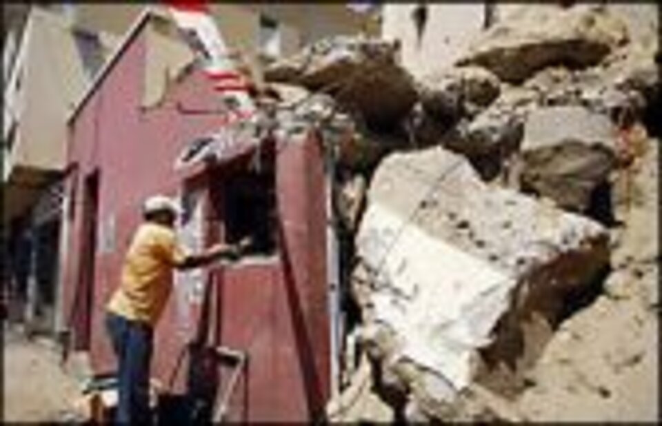 Foto: Ein Mann reicht einer Person in einem beschädigten Haus durch ein Fenster den Arm