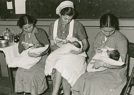 Historische Aufnahme: DRK - Krankenhaus in Busan (Südkorea): Koreanische Schwesternschülerinnen lernen Säuglingspflege und geben Säuglingen die Flasche. In der Mitte eine deutsche Lehrschwester.
