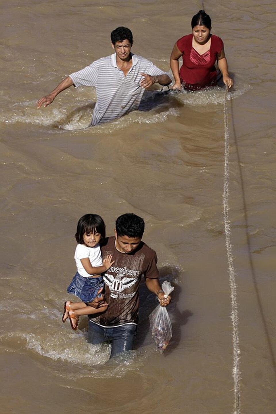 Foto: Ein junges Paar und ein Vater mit seiner Tochter auf dem Arm schreiten ducrh braune Wasserfluten.
