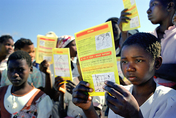 Foto: Eine Gruppe von Kindern halten Infoblätter vor ihren Gesichtern und lesen 