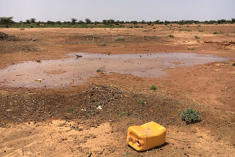 Pfützen in roter Erde mit Wasserkanister