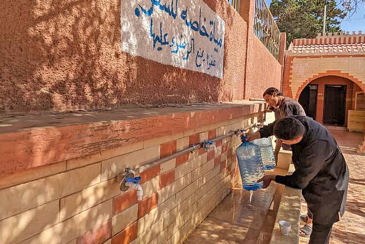 Zwei Personen füllen Flaschen mit Trinkwasser in Libyen 
