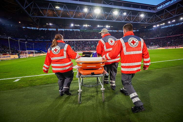 DRK-Sanitäterin und DRK-Sanitäter im Fußballsadion-Einsatz mit einer fahrbaren Krankentrage. 