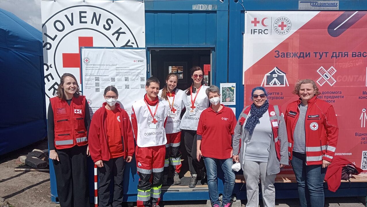 Acht Personen in den verschiedenen Dienstbekleidungen des Slowakischen Roten KReuzes, des DRK und des IKRK stehen in Vyšné Nemecké in der Slowakei vor einem Bürocontainer.