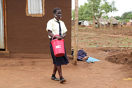 laufendes ugandisches Mädchen mit DRK-Eimer mit Hygiene-Kit