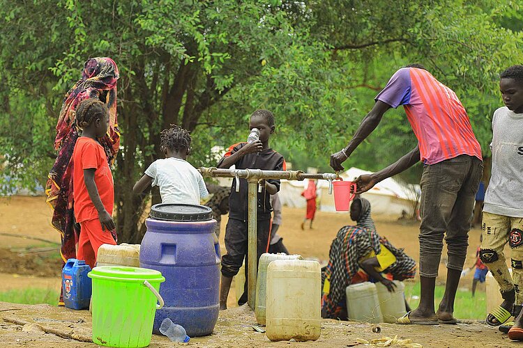 Familie an Wasserstelle trinkt und füllt Gefäß