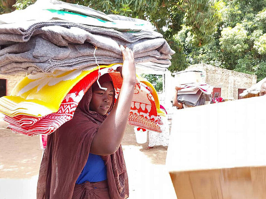 Geflüchtete Sudanesin trägt Decken vom Roten Kreuz