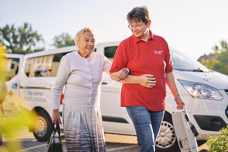 Seniorin und DRK-Pflegerin vor DRK-Bus