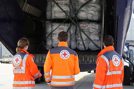 Rotkreuzmitarbeiter vor Transportmaschine mit Hilfsgütern