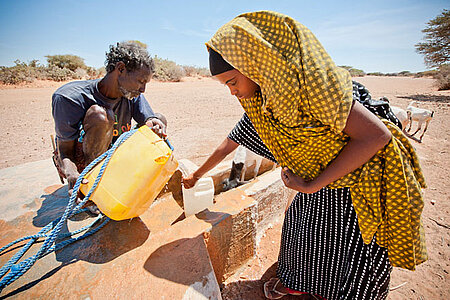 Foto: Ein Mann hilft einer jungen Frau in Somalia, Wasser in einen Kanister zu füllen